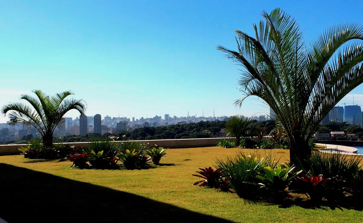 Jardín moderno con palmeras y vista a skyline urbano al fondo — proyecto Residência HC, por Gil Fialho