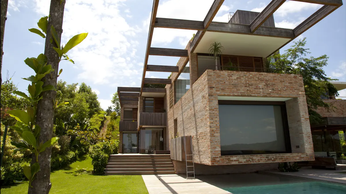 Casa contemporánea con fachada de ladrillo, pergola, pileta y jardín verde — proyecto Residência MP, por Gil Fialho