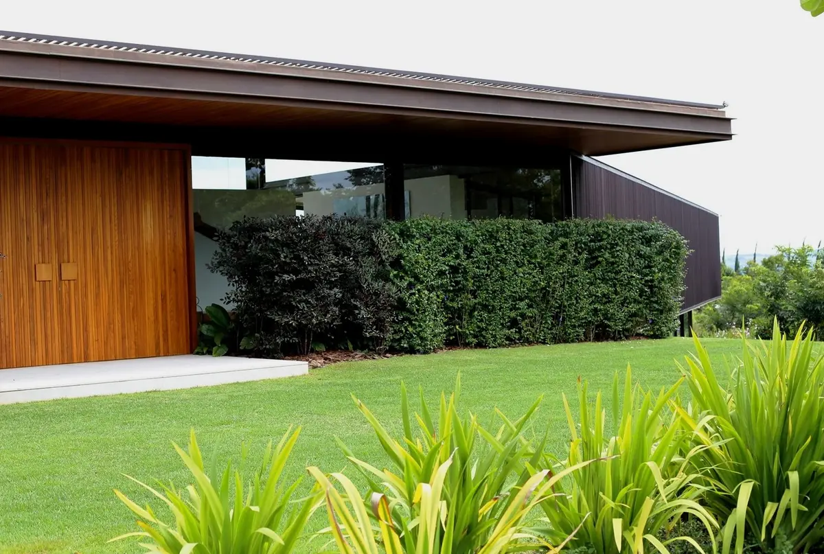 Casa contemporánea con fachada de madera, jardín verde y vegetación — proyecto Residência CA, por Gil Fialho