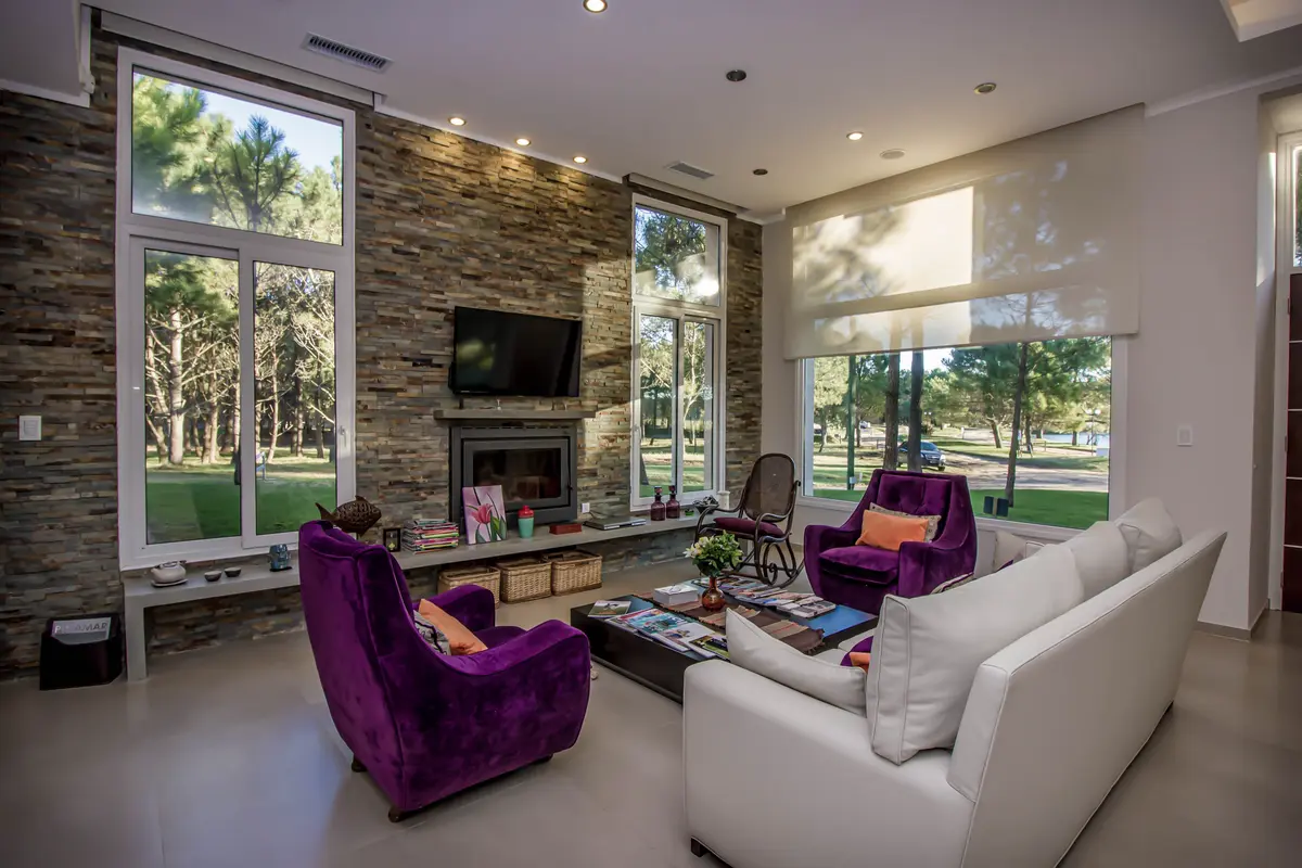 Sala de estar moderna com parede de pedra e poltronas roxas — projeto Vivienda Unifamiliar en Pinamar, por Estudio Schifano, em Pinamar