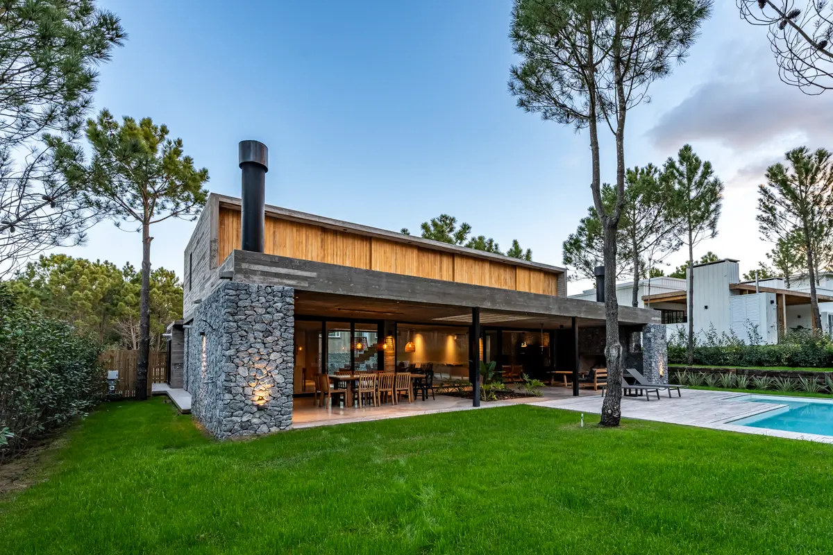 Fachada moderna com pedra, madeira e grandes janelas — projeto casa la huella, por Guerrero Arquitectos, em Pinamar