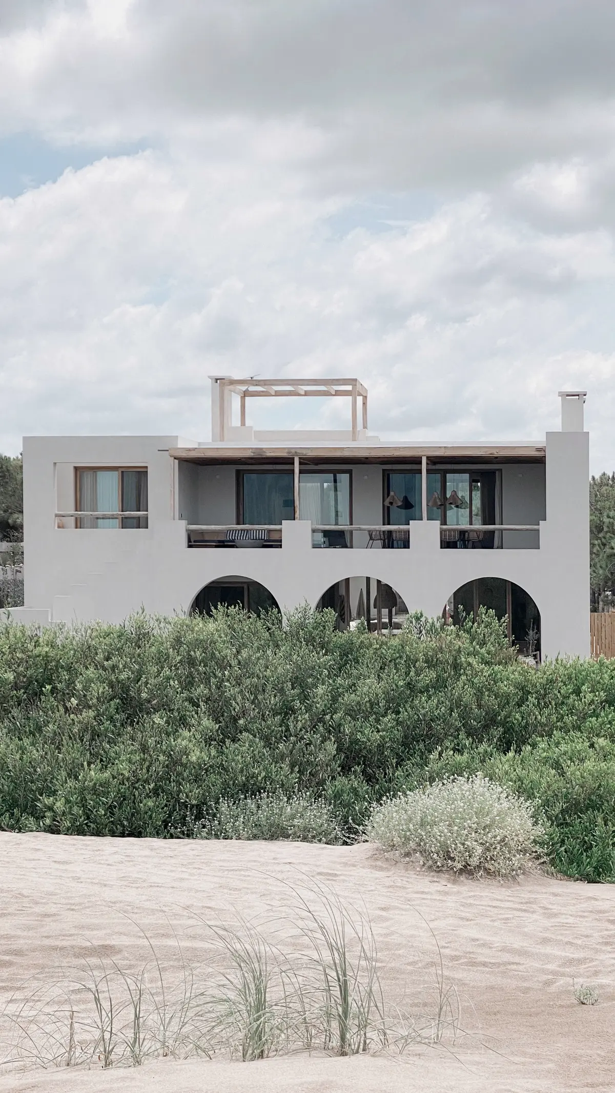 Casa branca moderna mediterrânea com arcos e vegetação costeira — projeto El Refugio, por Grupo Pauta Arquitectura, em Pinamar