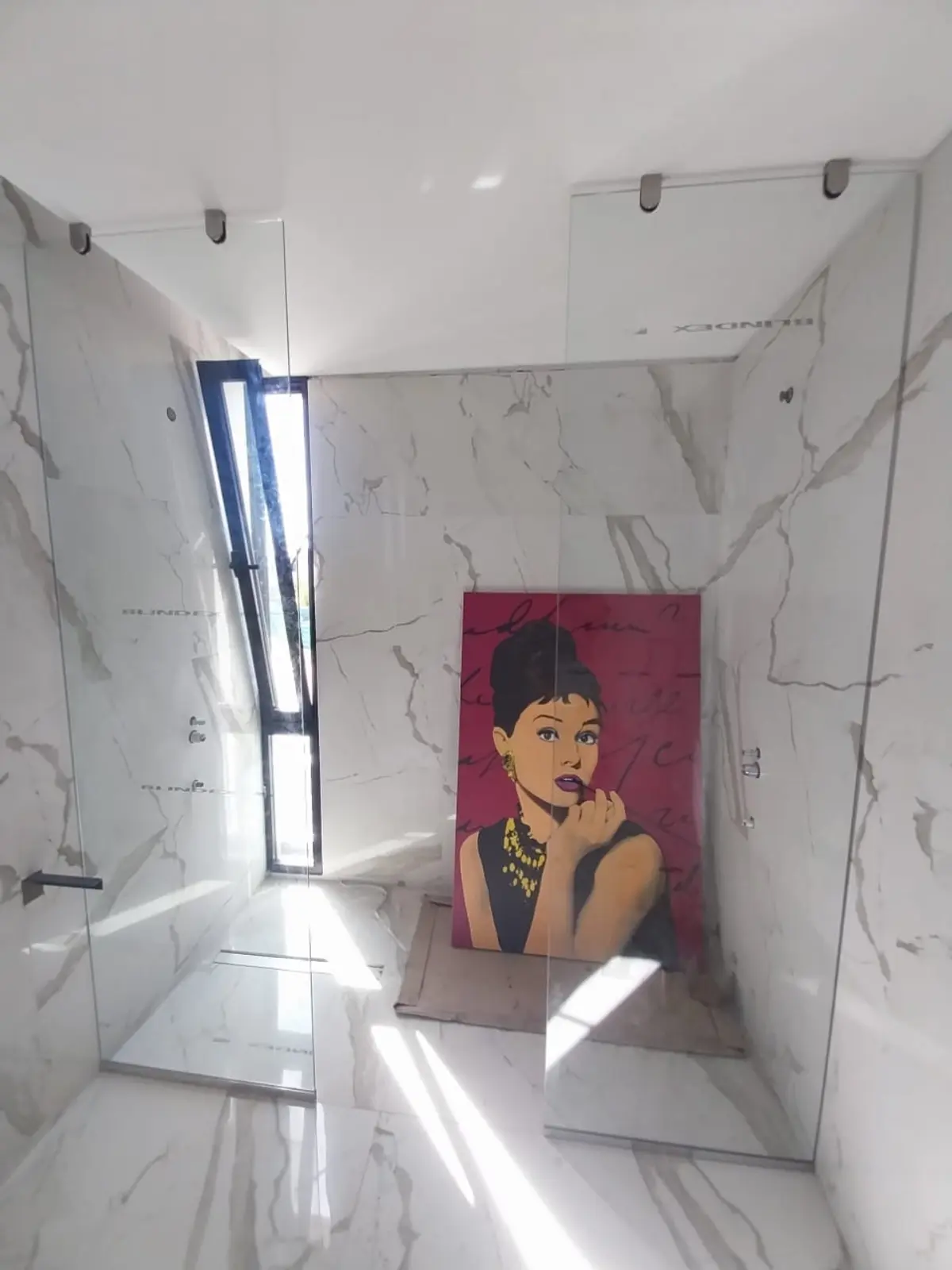 Banheiro moderno com paredes de mármore, obra de arte de Audrey Hepburn e box de vidro — projeto Mamparas paños fijos con clip acero, por Cristalcenter, em Belén de Escobar