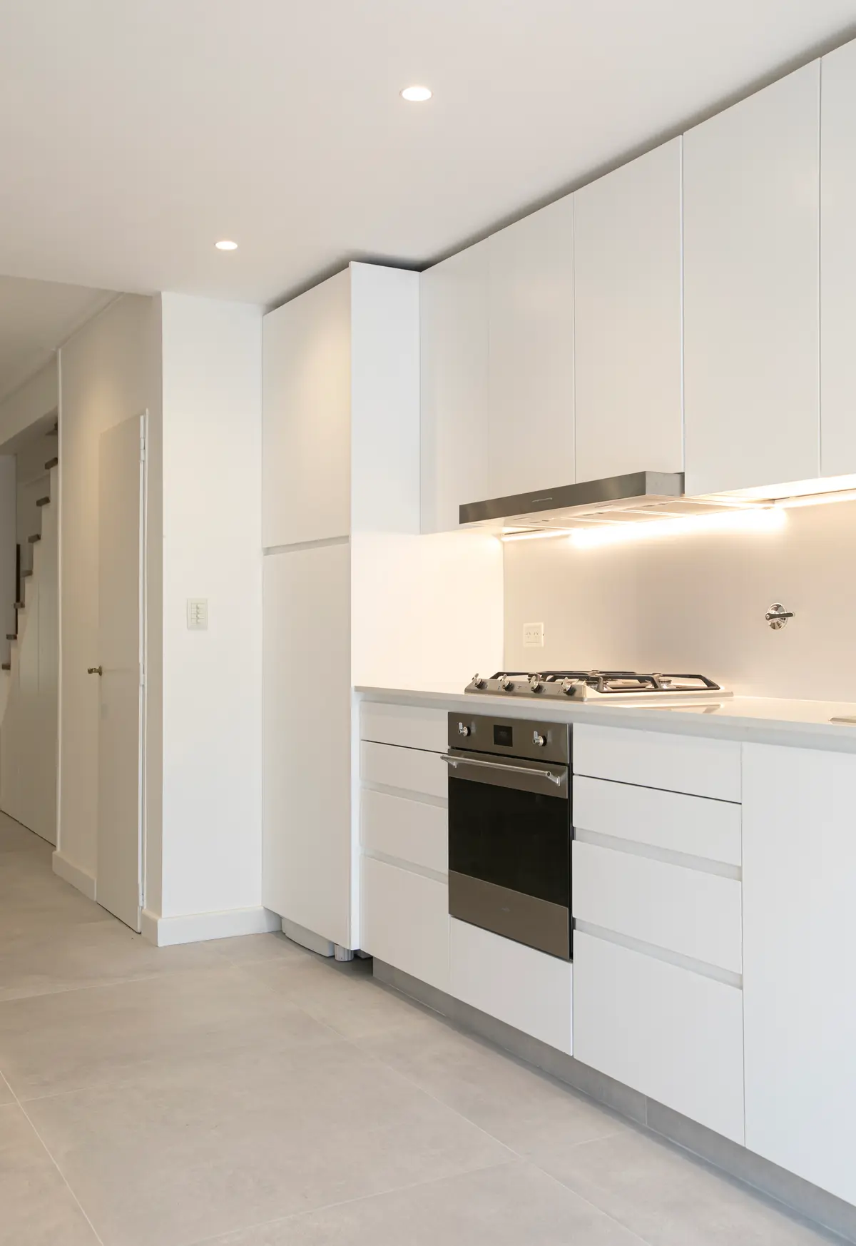 Cozinha moderna minimalista com armários brancos e piso de pedra cinza — projeto Obra Martinez A, por Arq. Lourdes Yarade Saravia, em Martínez