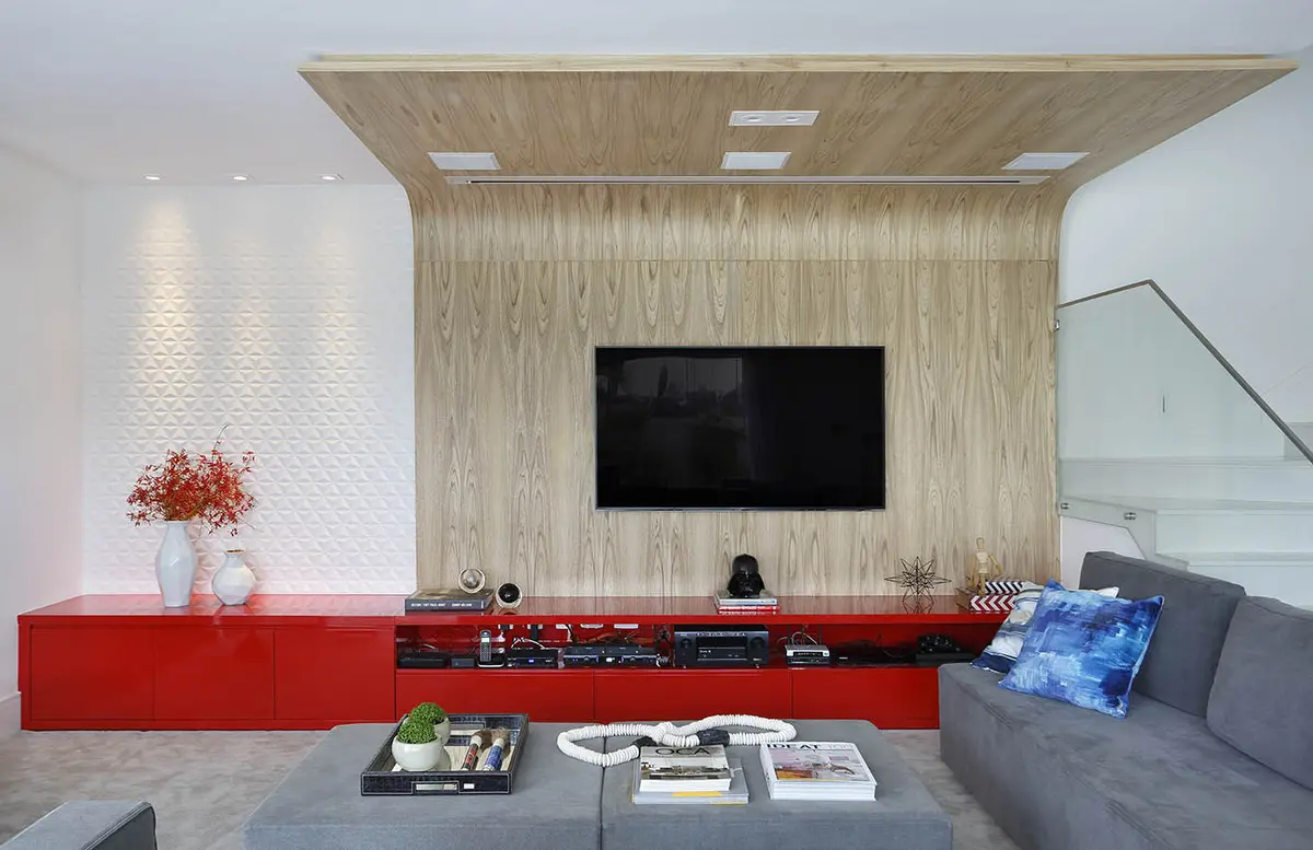 Living moderno con pared de madera, TV empotrada y mueble rojo — proyecto Casa Blue House, por Amanda Miranda