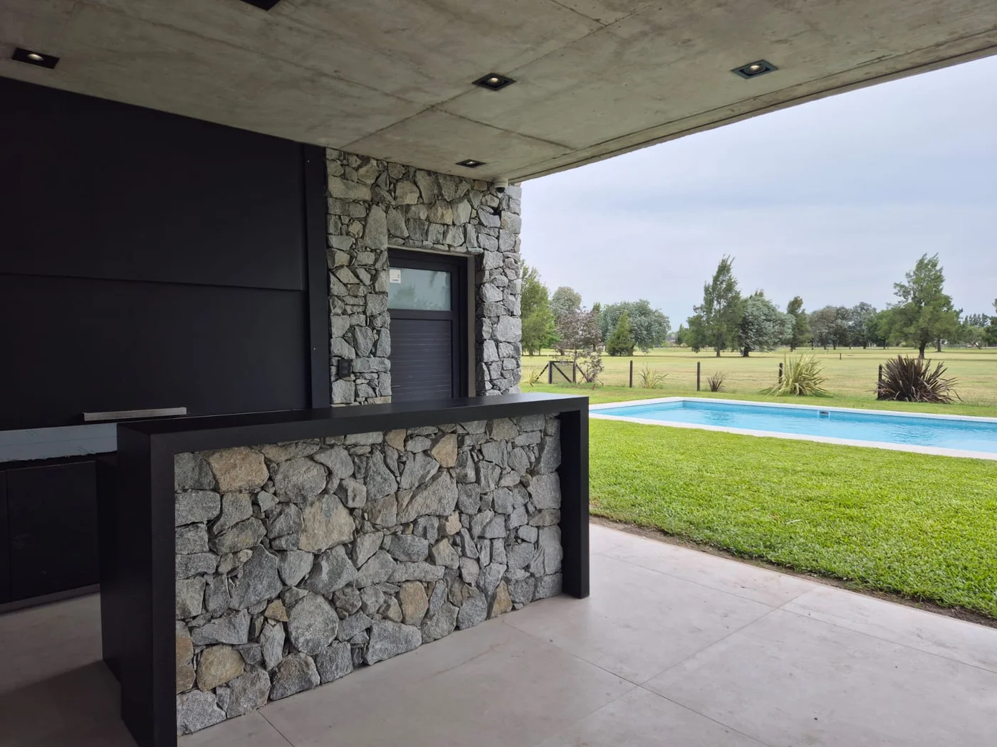 Galería moderna con pileta, piedra y vistas al campo verde.
