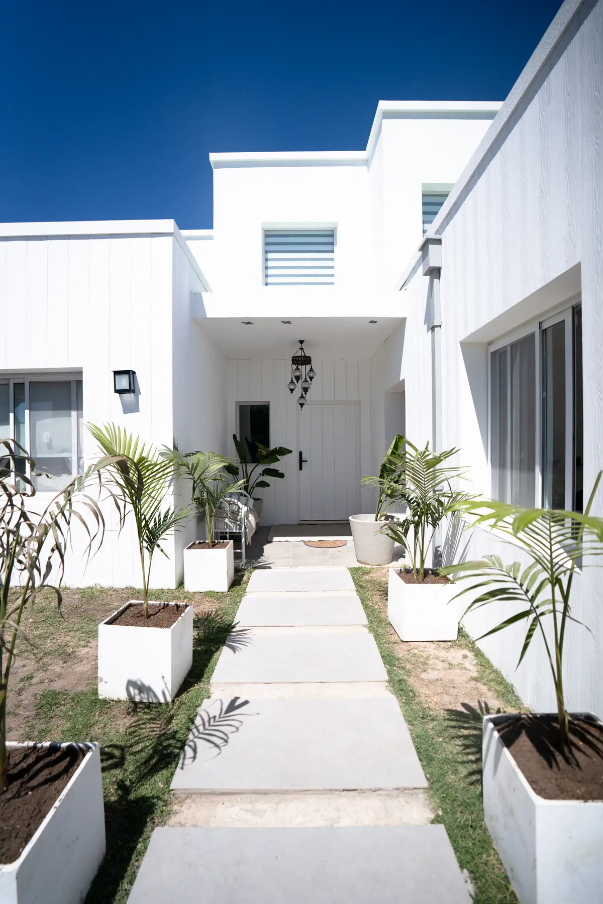 Fachada moderna blanca con camino de cemento y plantas — proyecto Obra Fachada Nicole, por Arq. Lourdes Yarade Saravia, en Manzanares