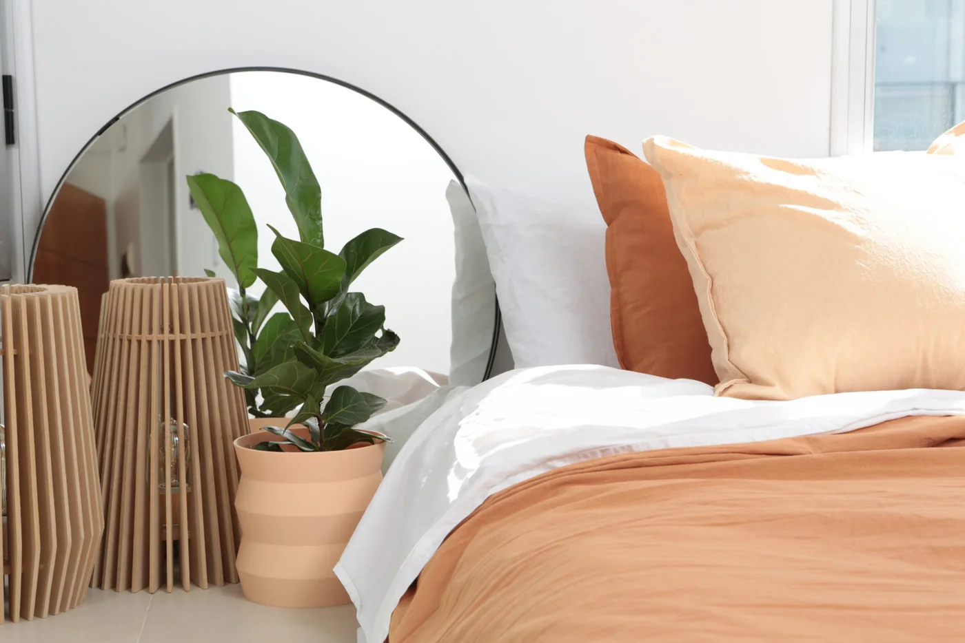 Dormitorio con cama, espejo redondo y lámparas de ratán.