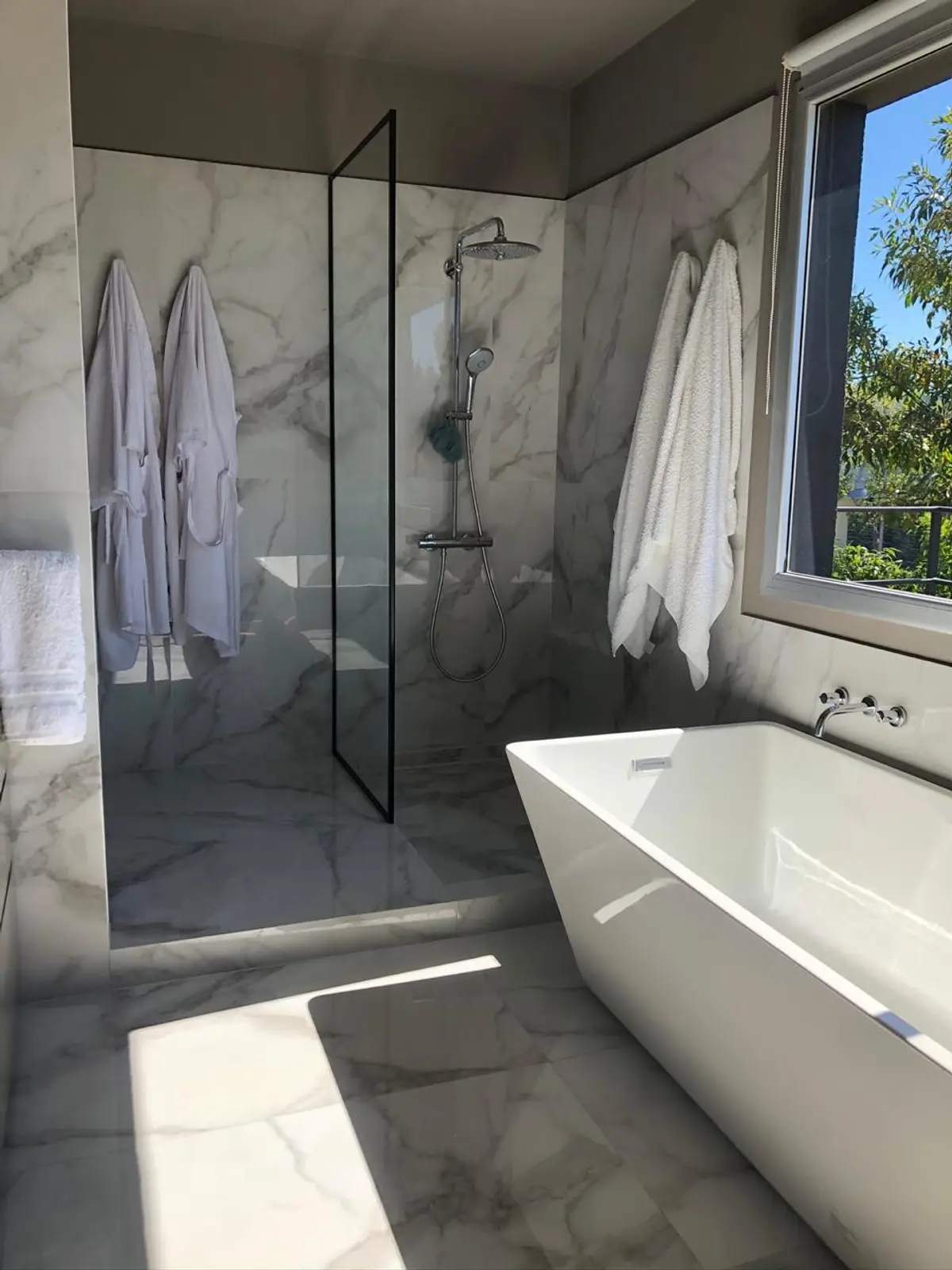 Banheiro moderno com banheira freestanding, box de vidro e paredes de mármore — projeto Casa Nordelta, por Etude Interiorismo, em Nordelta