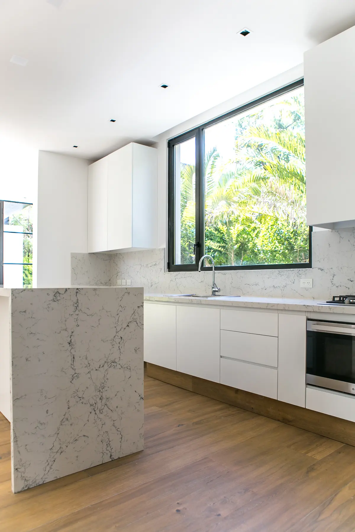 Moderna cocina blanca con isla de mármol y ventanal al jardín — proyecto Bosque Chico, por Estudio Arq. María Sioli, en Garin
