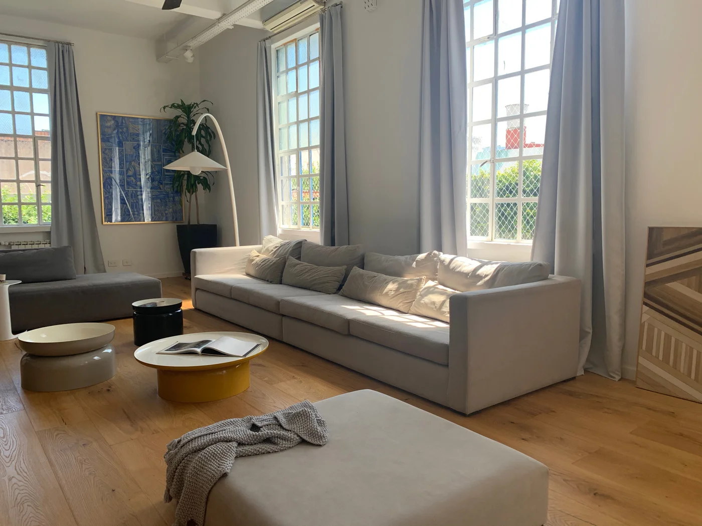 Living moderno con sofá gris, ventanas amplias y piso de madera.