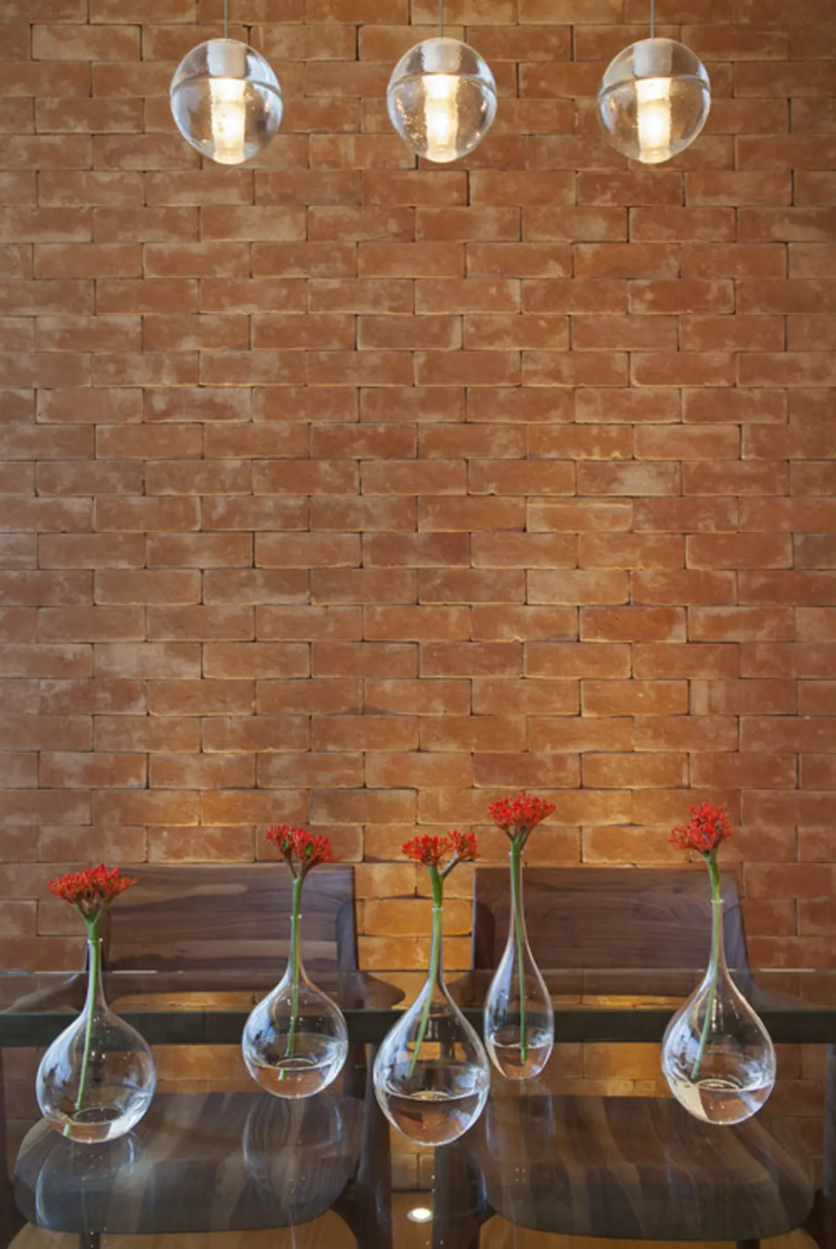 Pared de ladrillo con floreros con claveles rojos sobre mesa oscura — proyecto MS House, por Studio Ro-ca