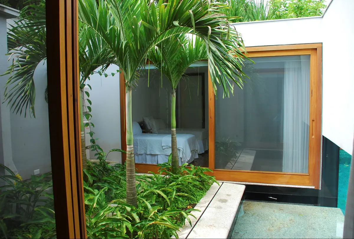 Patio interior con plantas, ventanales de madera y dormitorio visible — proyecto Residência MI, por Gil Fialho