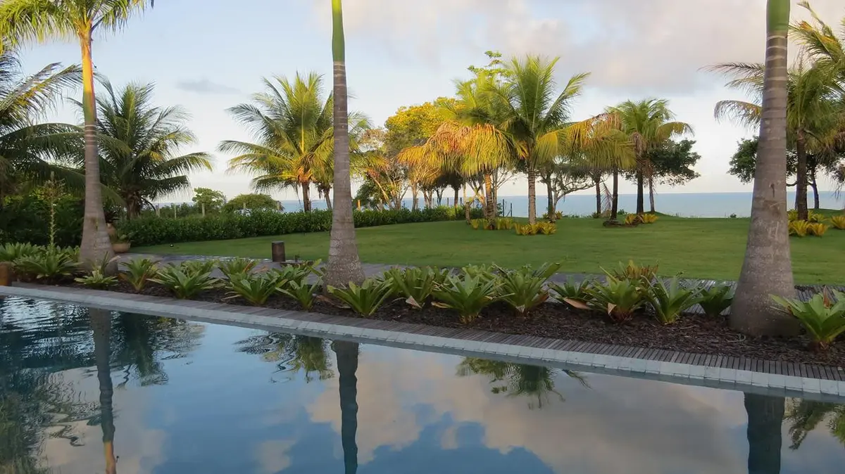 Patio con pileta reflectante, palmeras y terraza con vista al mar — proyecto Trancoso II, por Gil Fialho