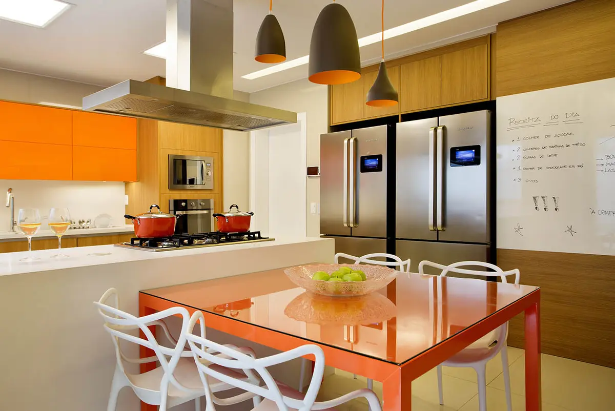Comedor moderno con mesa naranja, cocina integrada y lámparas colgantes — proyecto Casa Blue House, por Amanda Miranda