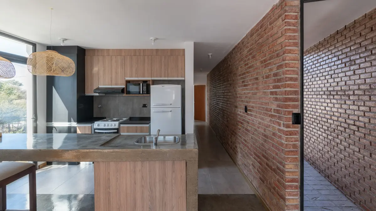 Cozinha moderna com ilha, parede de tijolos aparentes e acabamentos em madeira — projeto Casa 2/3, por Momento.