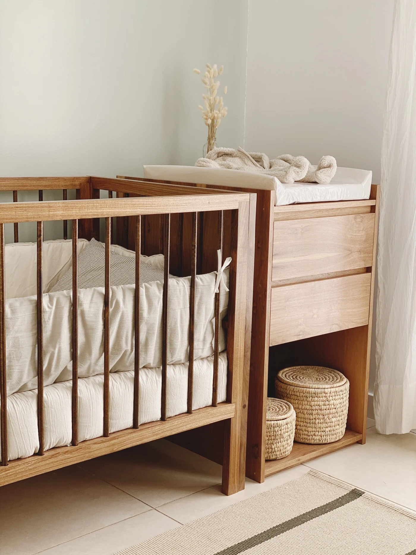 Cuna de madera natural con cajonera y cestas de mimbre.