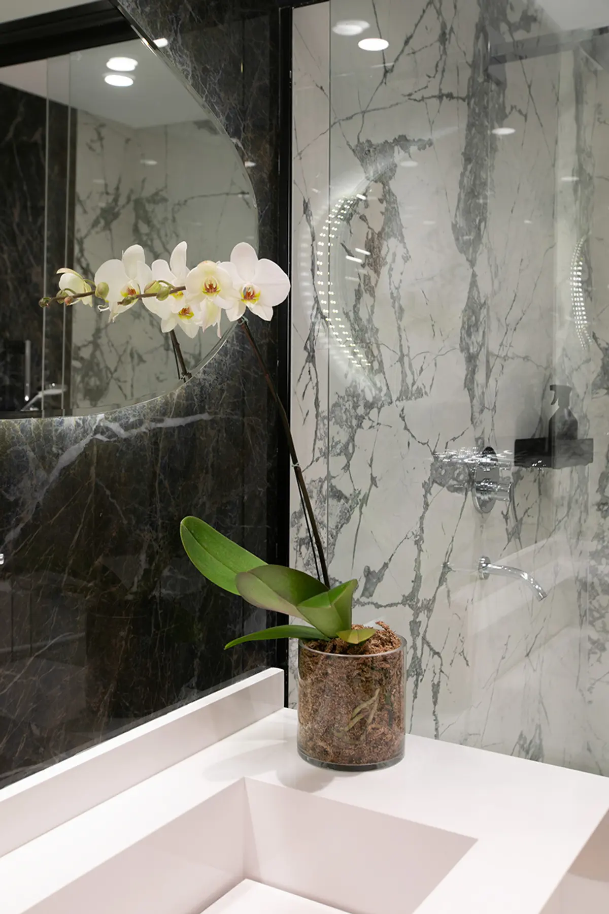 Orquídea blanca en baño moderno con mármol gris y espejo — proyecto Casa Oroño, por Estudio Plats, en Buenos Aires