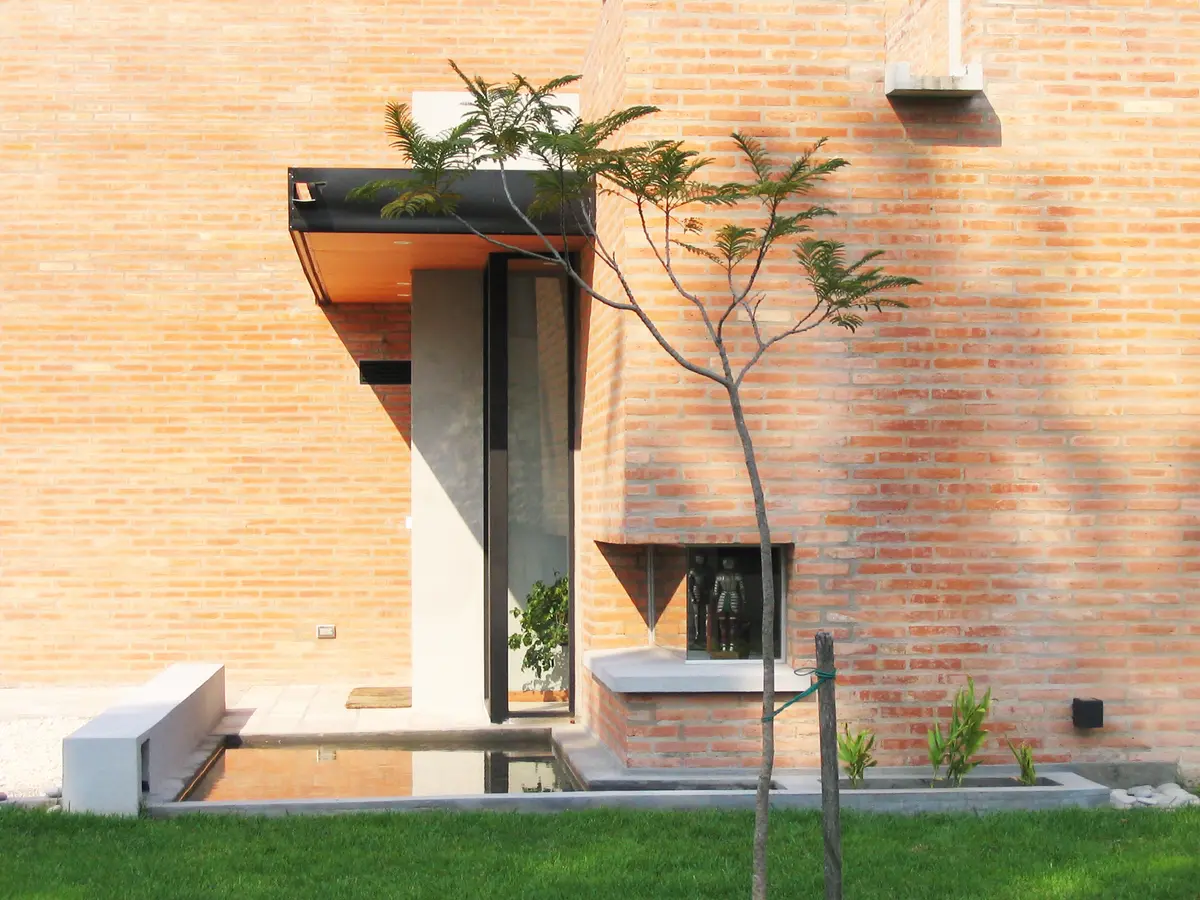 Fachada moderna com tijolo aparente, concreto e uma pequena árvore — projeto Casa Markelin - Barrio Laguna del Sol (Tigre, Buenos Aires) German Salas arquite, por German Salas arqu