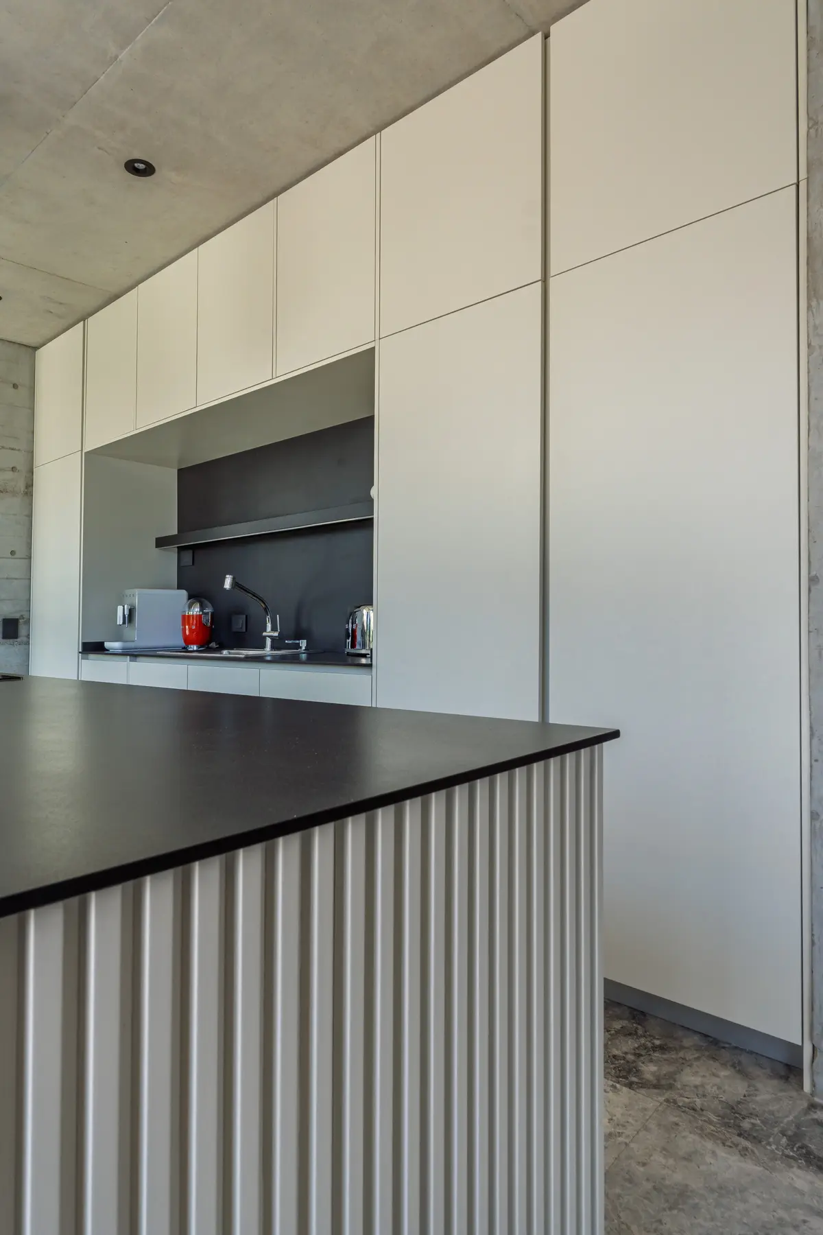 Cocina moderna con muebles blancos, encimera negra y detalles de hormigón — proyecto La Martona - Estudio Barcelona, por ABEJA CONCEPT, en Cañuelas