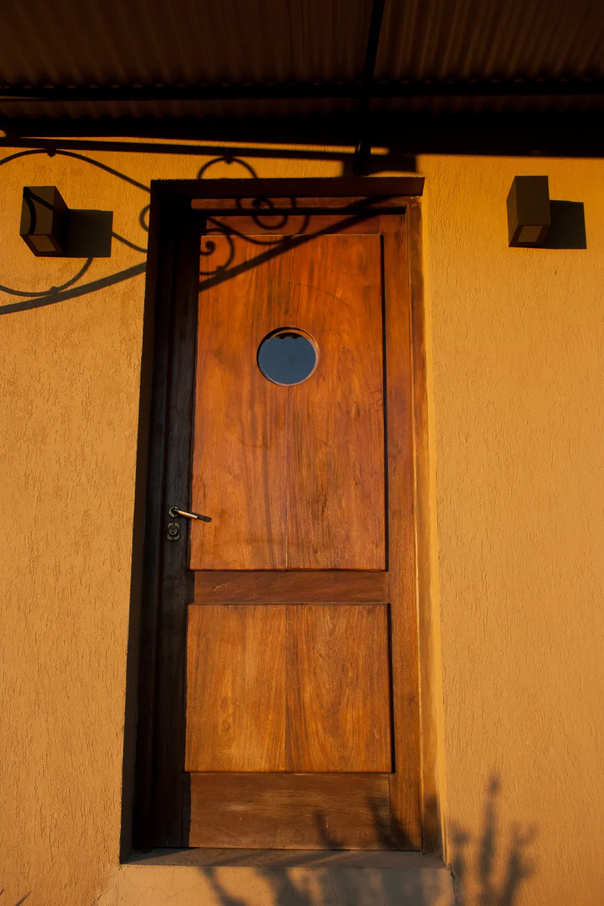 Porta rústica de madeira com janela redonda e parede terracota — projeto Inmuebles, por Geo Estudio, em Buenos Aires