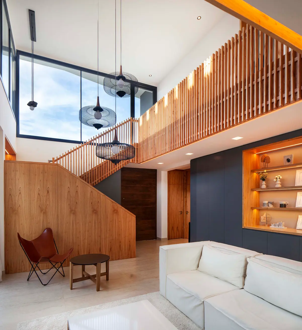 Interior moderno de pé-direito duplo com escada flutuante e painel de ripas de madeira — projeto Castaños, por GO arquitectos, em Rincón de Milberg