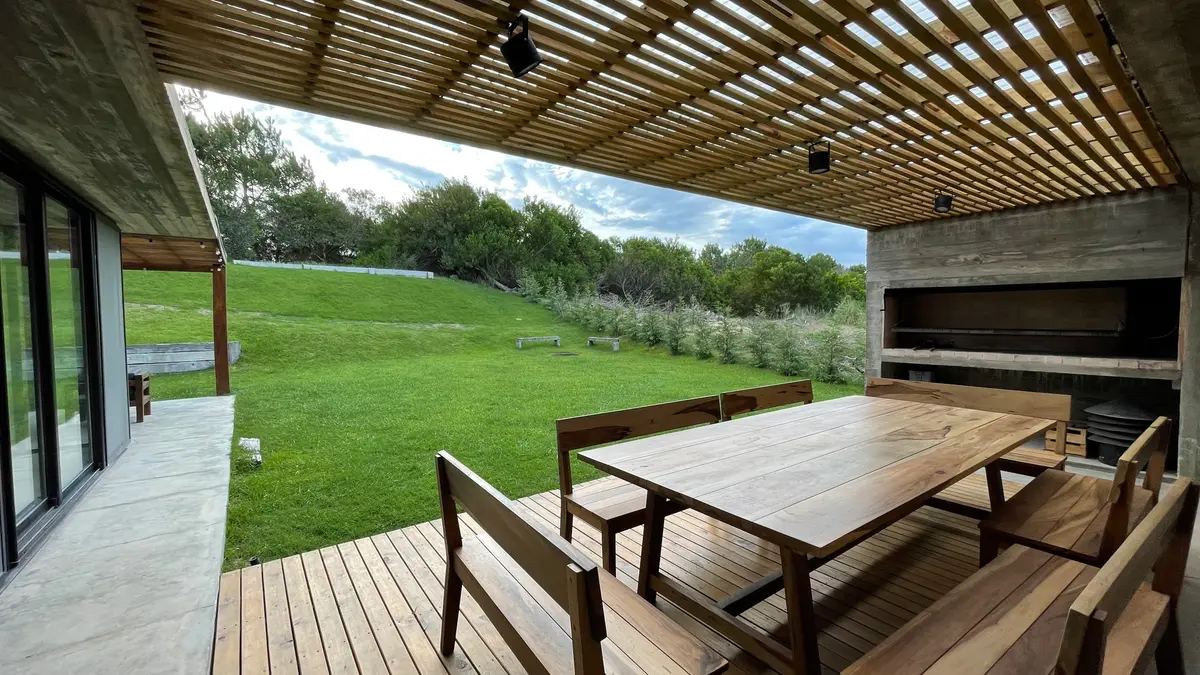 Sala de jantar externa com deck, pergolado de madeira e gramado — projeto Casa R2, por Guerrero Arquitectos, em Pinamar