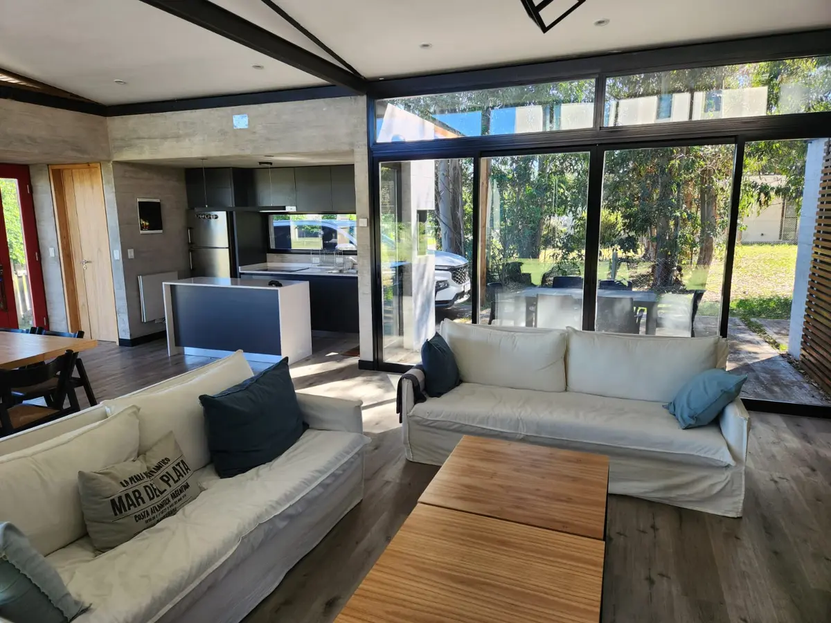 Sala moderna com janelas amplas, vigas de madeira e vista para floresta — projeto Casa Arenas del Sur, por Arq Fernando Ossvald, em Mar del Plata