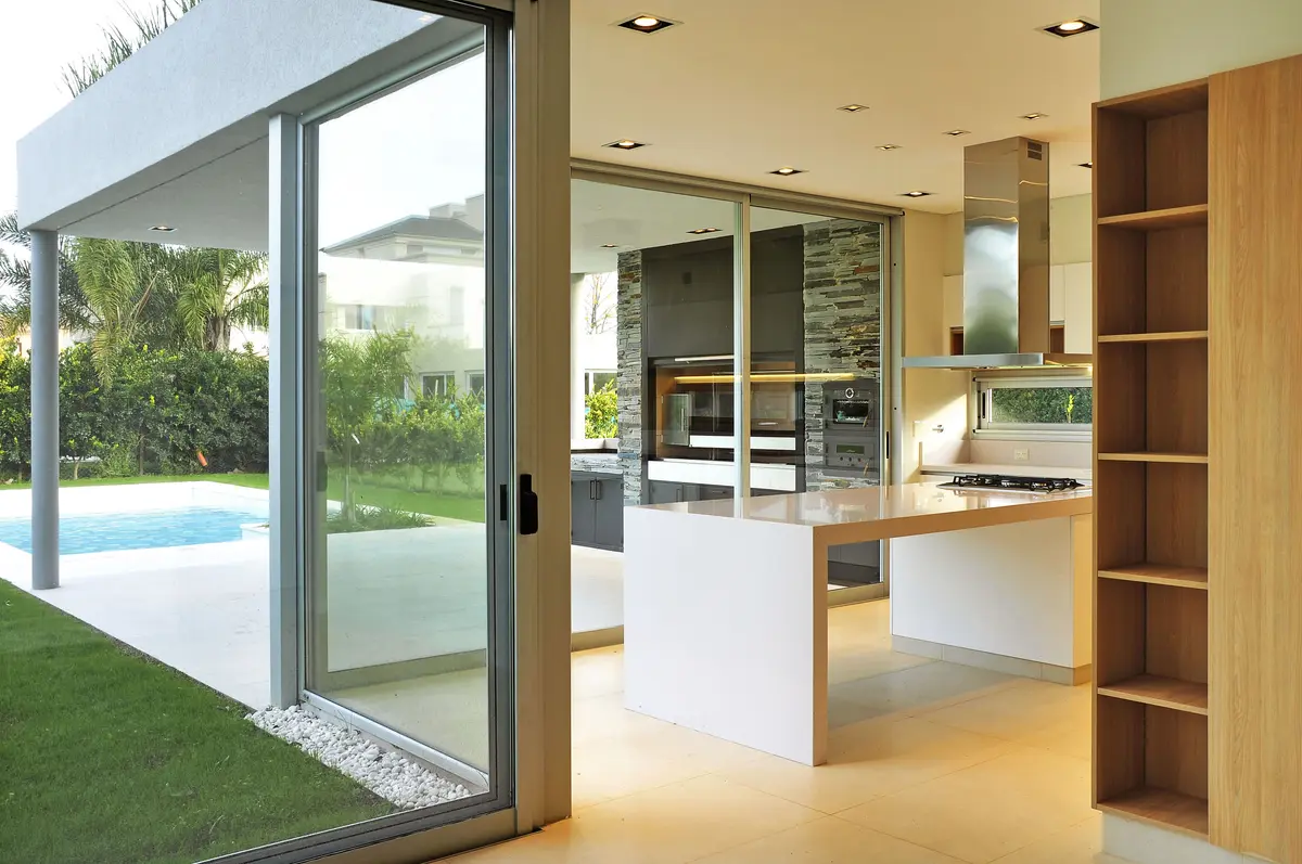 Cozinha moderna integrada com ilha e vista para piscina e jardim — projeto Casa EP, por Santiago Cordeyro Arquitectos, em Del Viso