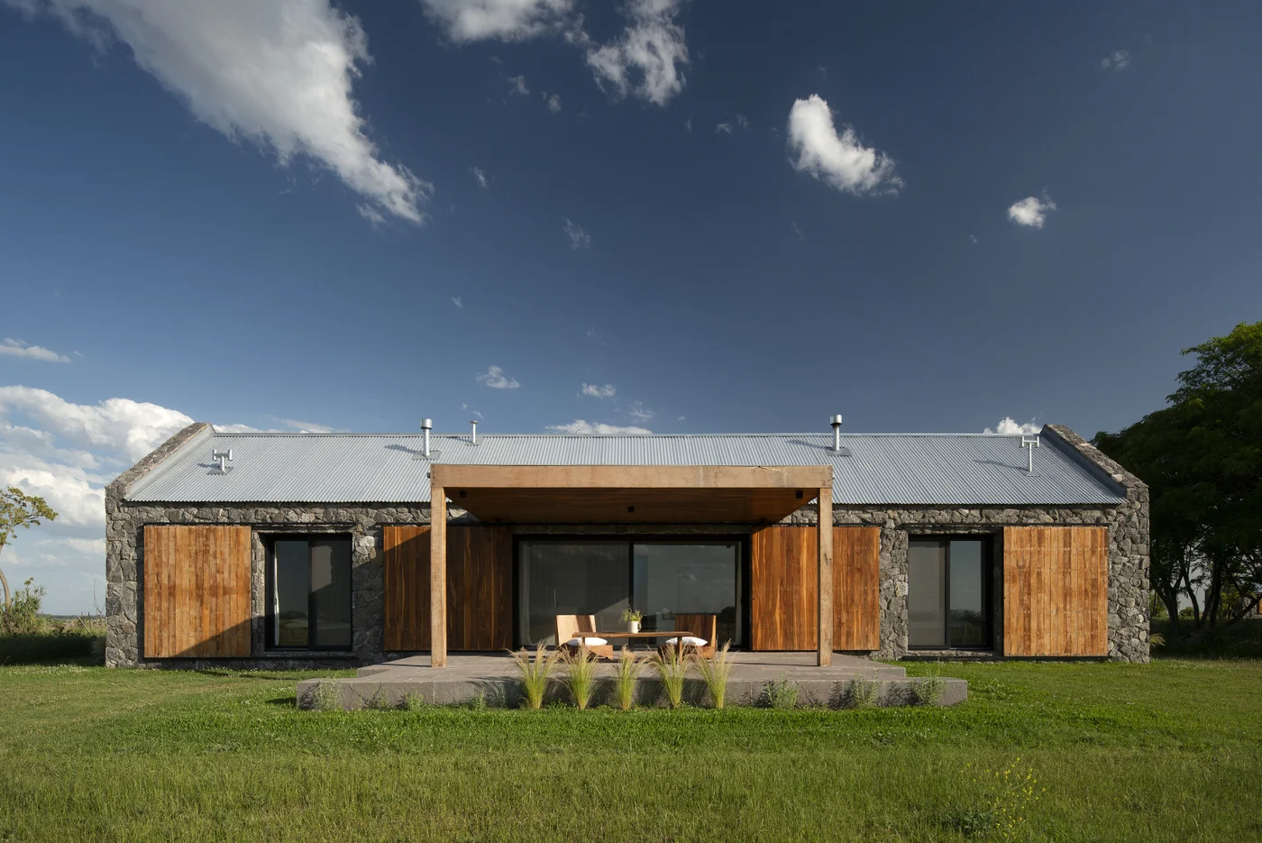 Fachada moderna de piedra y madera con pérgola y patio central
