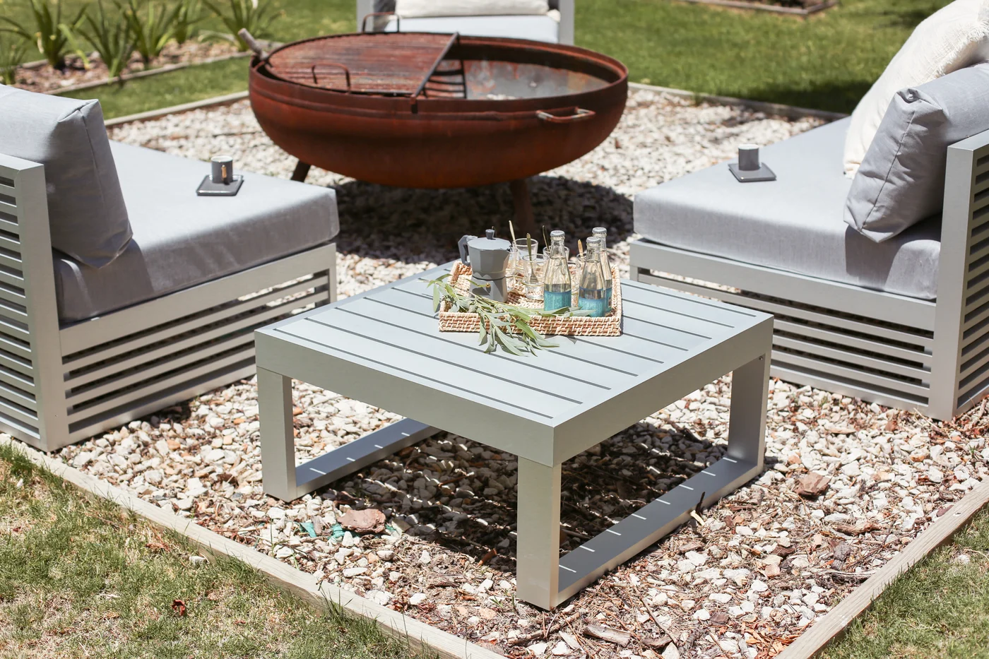 Patio con hogar circular, sillones grises y mesa baja de madera.