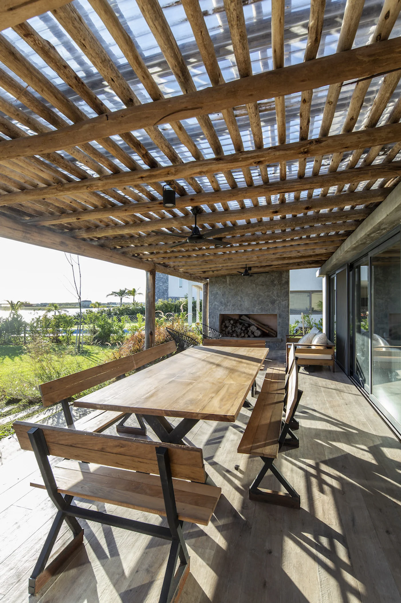 Galería con pergola de madera, mesón y hogar, vista al jardín