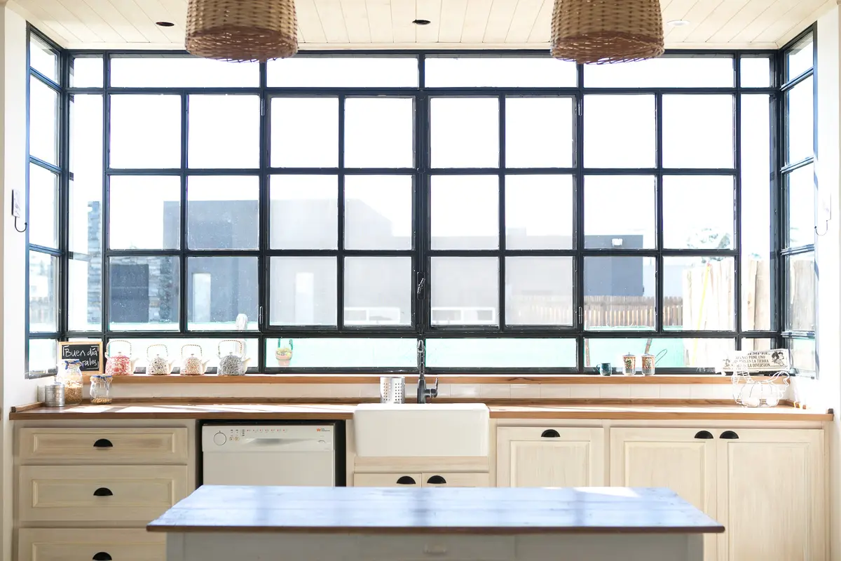 Cozinha moderna com janela industrial e armários de madeira — projeto Santa Teresa, por Atelier Doucet, em Benavidez