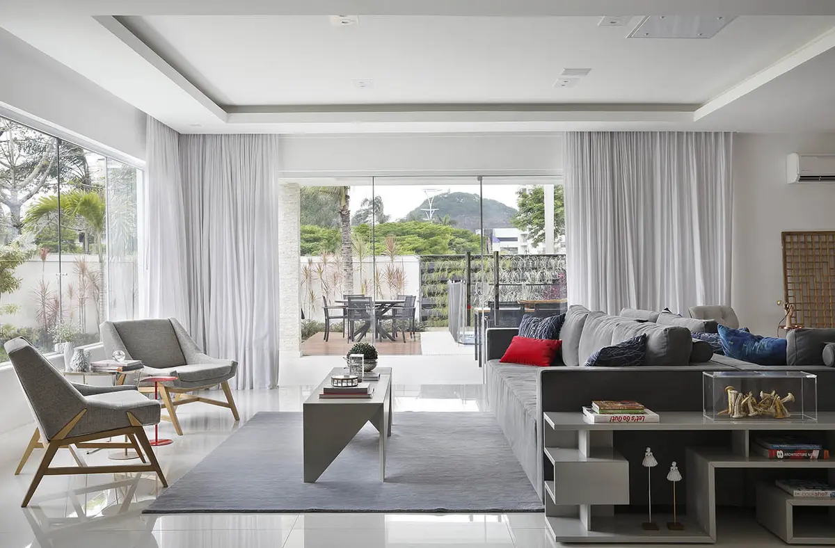 living moderno con ventanales, sillones grises y vista al jardín — proyecto Casa Blue House, por Amanda Miranda