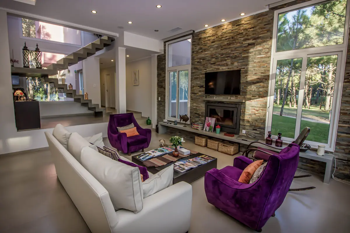 Living moderno con pared de piedra y sillones violetas — proyecto Vivienda Unifamiliar en Pinamar, por Estudio Schifano, en Pinamar