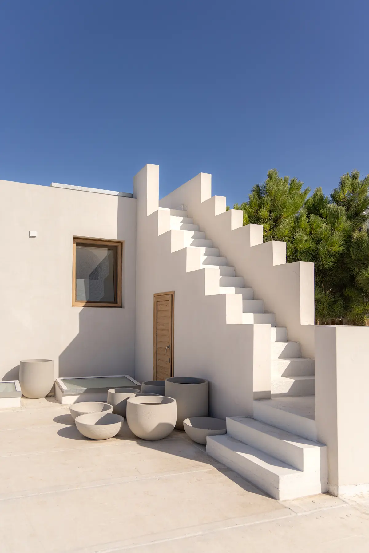 terraço minimalista com escadas brancas e vasos de concreto — projeto El Refugio, por Grupo Pauta Arquitectura, em Pinamar