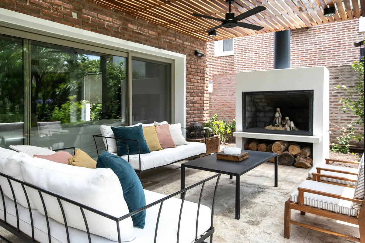 Patio moderno con sala de estar interior-exterior, chimenea y pérgola — proyecto Obra La Posta, por Arq. Lourdes Yarade Saravia, en Pilar
