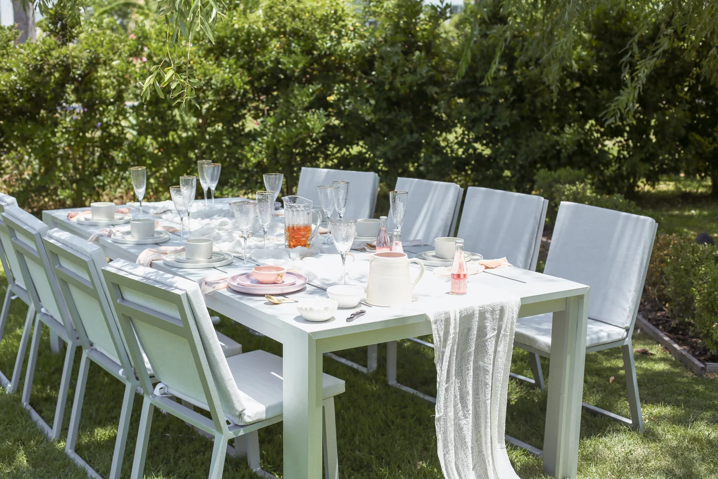 mesa comedor blanca con sillas en jardin bajo pergola arbolada