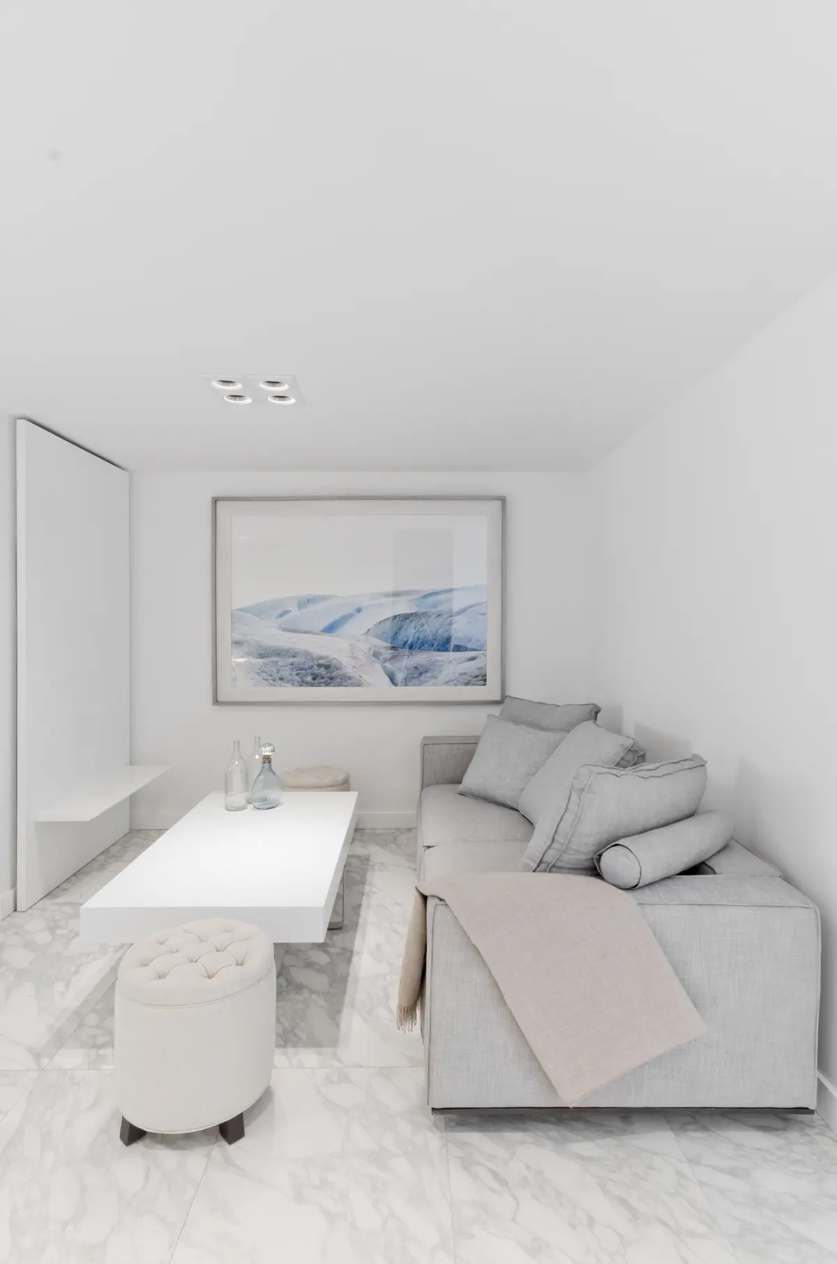 Living minimalista con sofá gris, mesa blanca y suelo de mármol — proyecto Departamento Nuñez, por Claudia Faena Studio, en Núñez