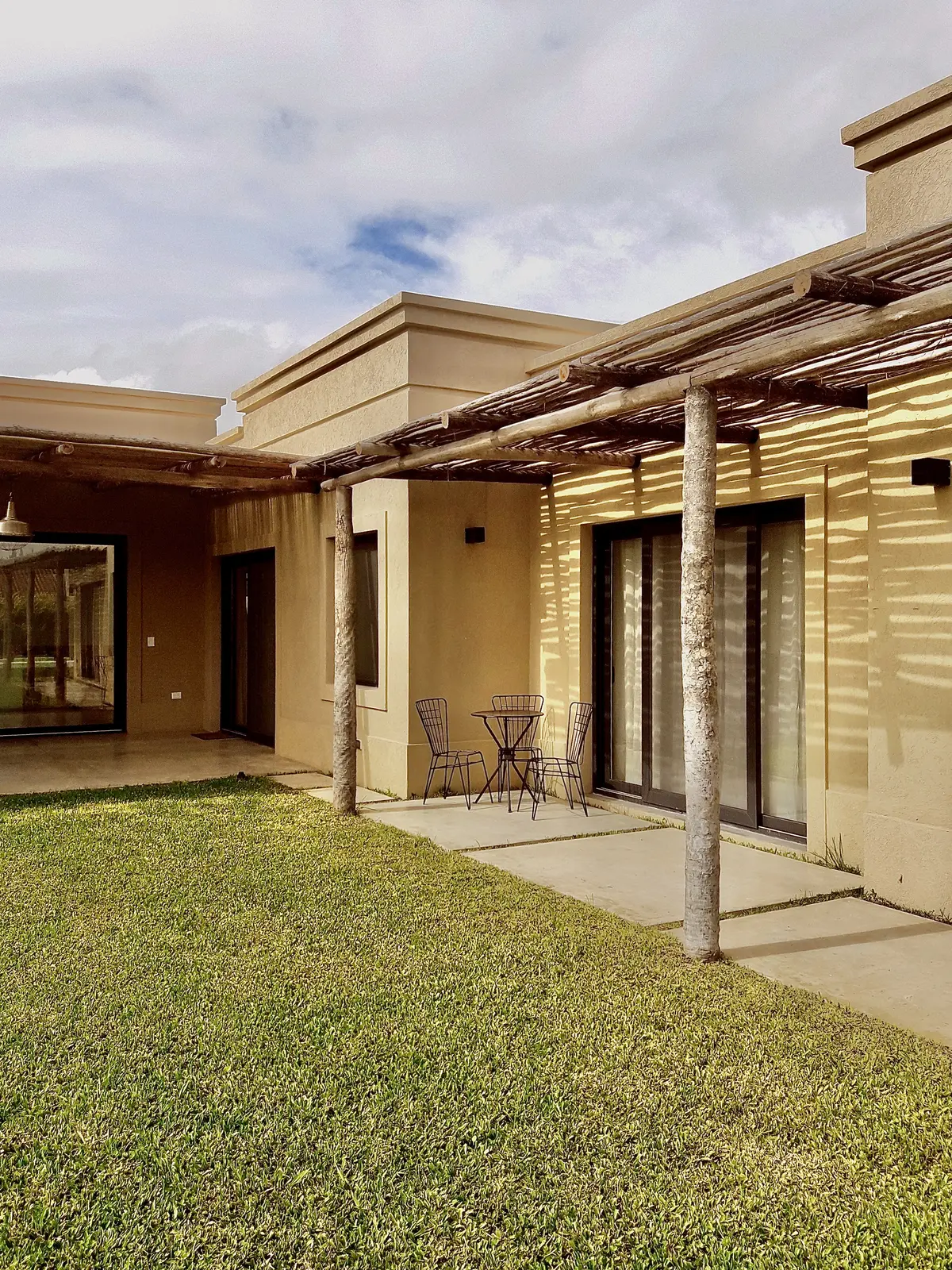Patio exterior con césped, galería de pérgola y mobiliario de hierro — proyecto Santa Teresa 2, por Marconi Silva Arquitectos, en Benavidez