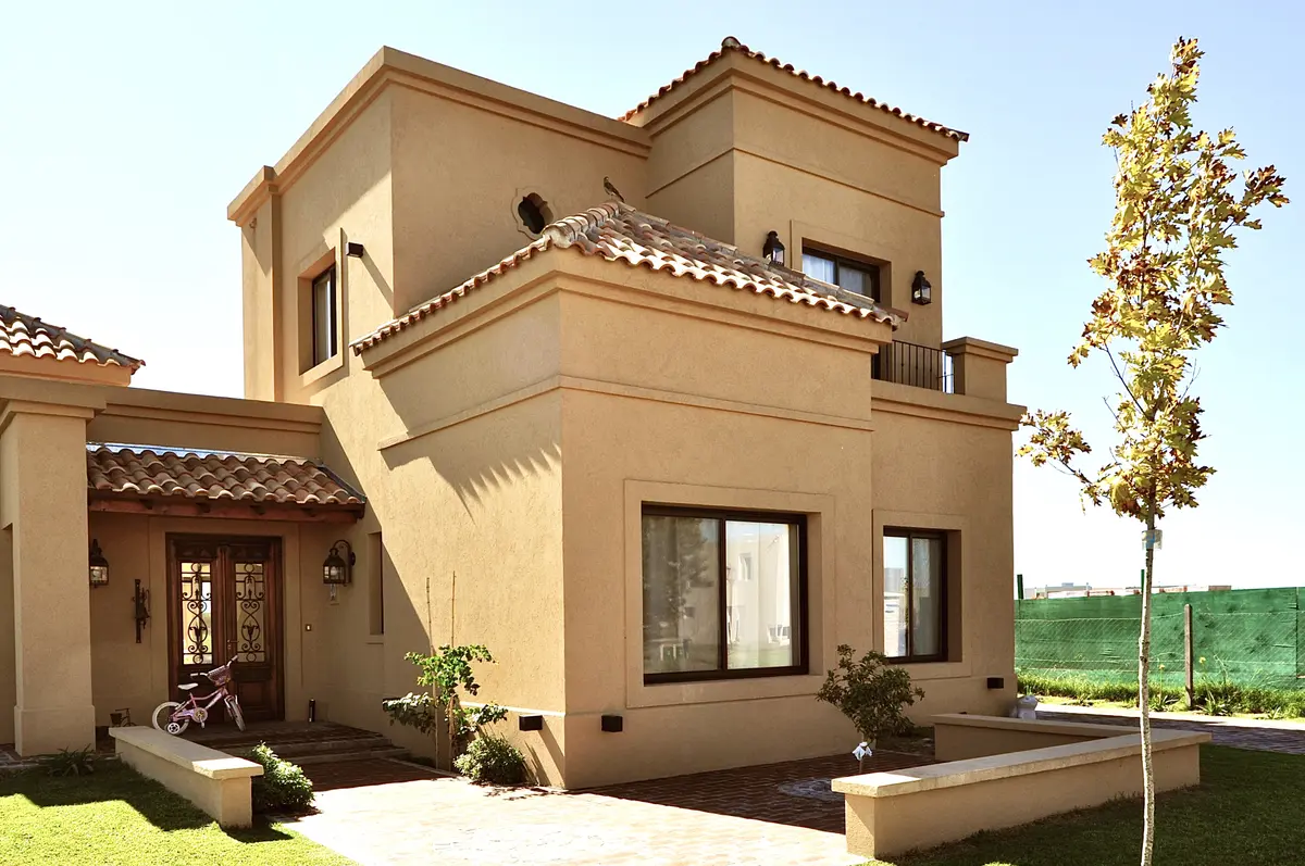 Fachada residencial estilo mediterrâneo bege com telhados de terracota e jardim — projeto San Marcos, por Marconi Silva Arquitectos, em Benavidez
