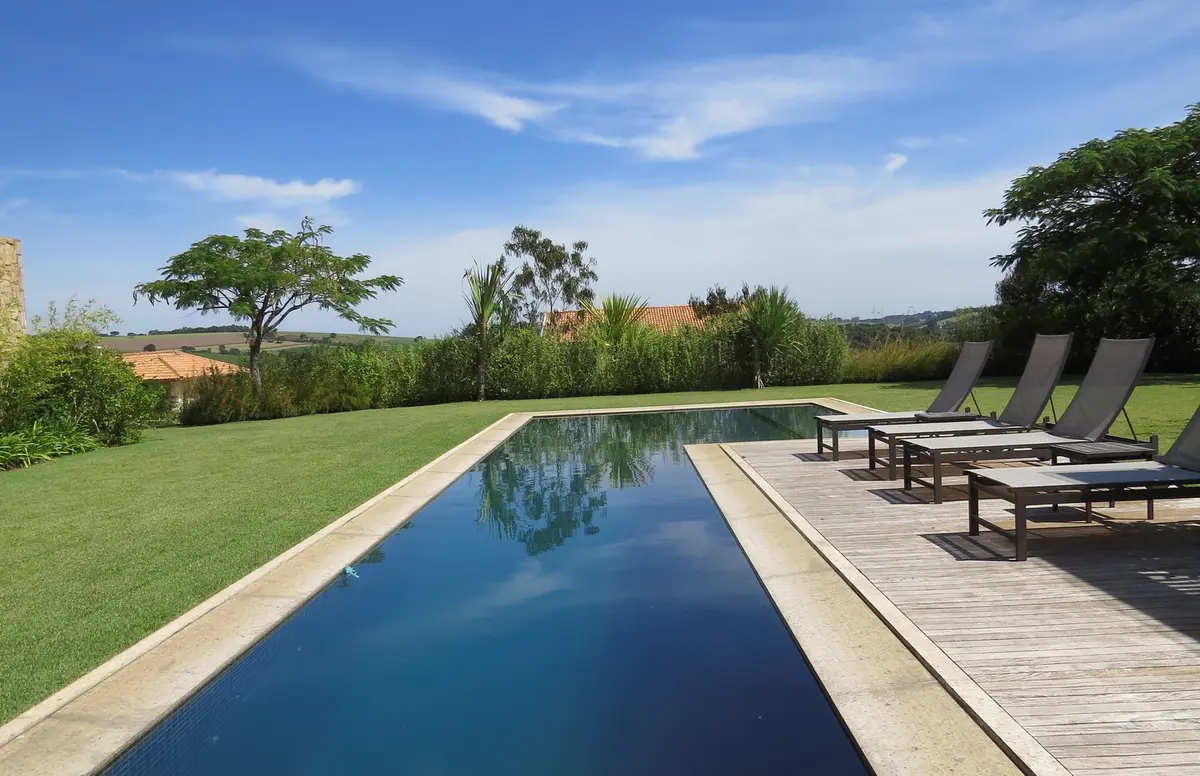 Pileta espejo con deck de madera y jardín verde extenso — proyecto Residencia PZ, por Gil Fialho