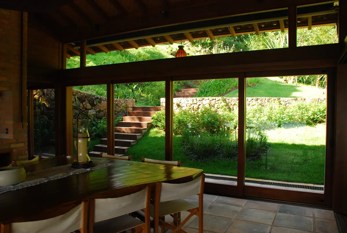 Galería abierta con ventanales hacia jardín y pérgola de madera — proyecto Fazenda Indaiauba, por Gil Fialho