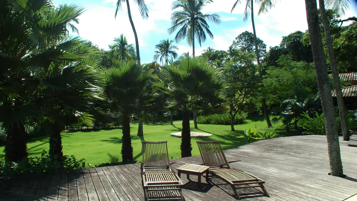Terraza de madera con reposeras frente a jardin verde y palmeras — proyecto Residência RC, por Gil Fialho