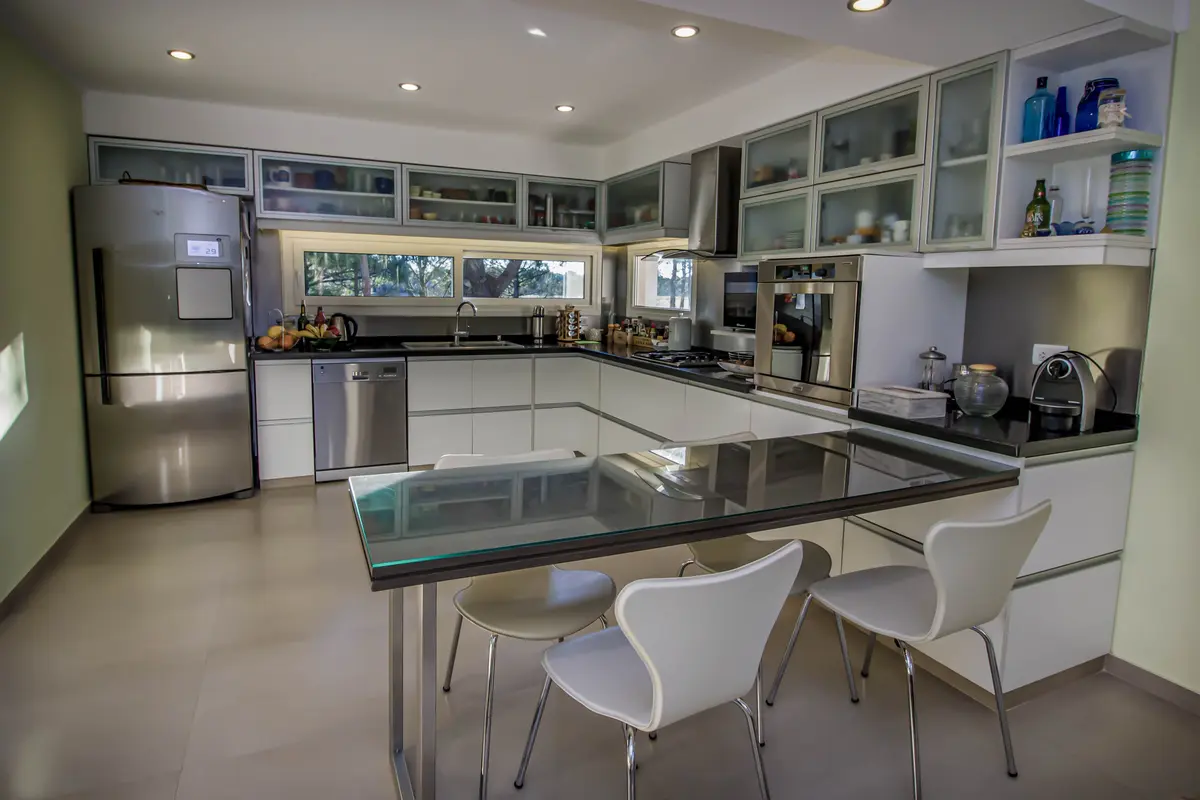 Cozinha moderna, ampla e branca com ilha e cadeiras de design — projeto Vivienda Unifamiliar en Pinamar, por Estudio Schifano, em Pinamar