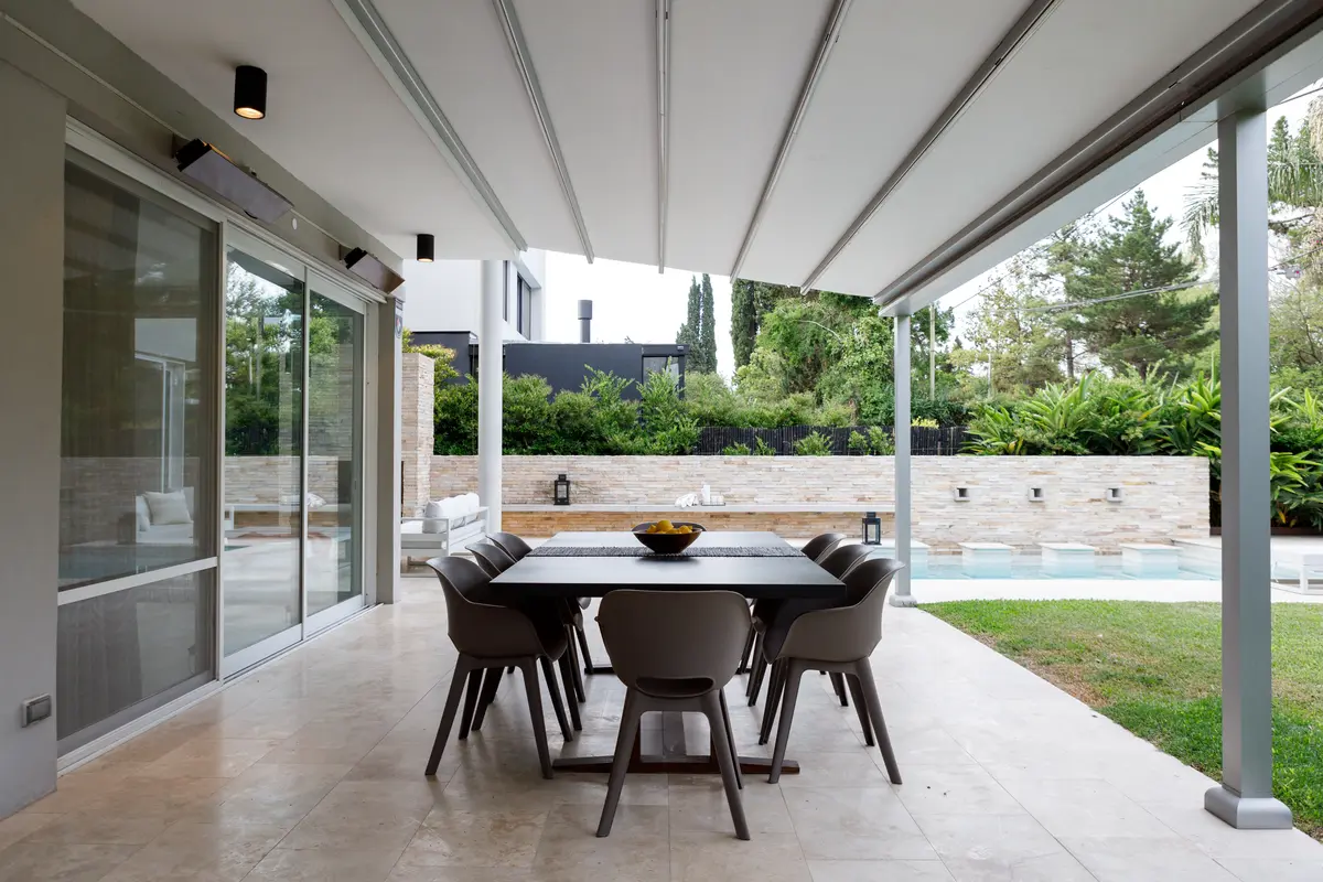 Área de jantar externa moderna com mesa de madeira escura e cadeiras cinzas sob toldo retrátil — projeto TOLDER - PERGOLAS, por Argentina en Obra 2024, em Rincón de Milberg