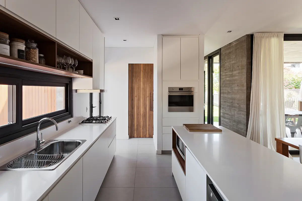 Cozinha moderna com ilha branca, armários de madeira e muita luz — projeto CASA RDV, por Rastro Estudio, em San Isidro