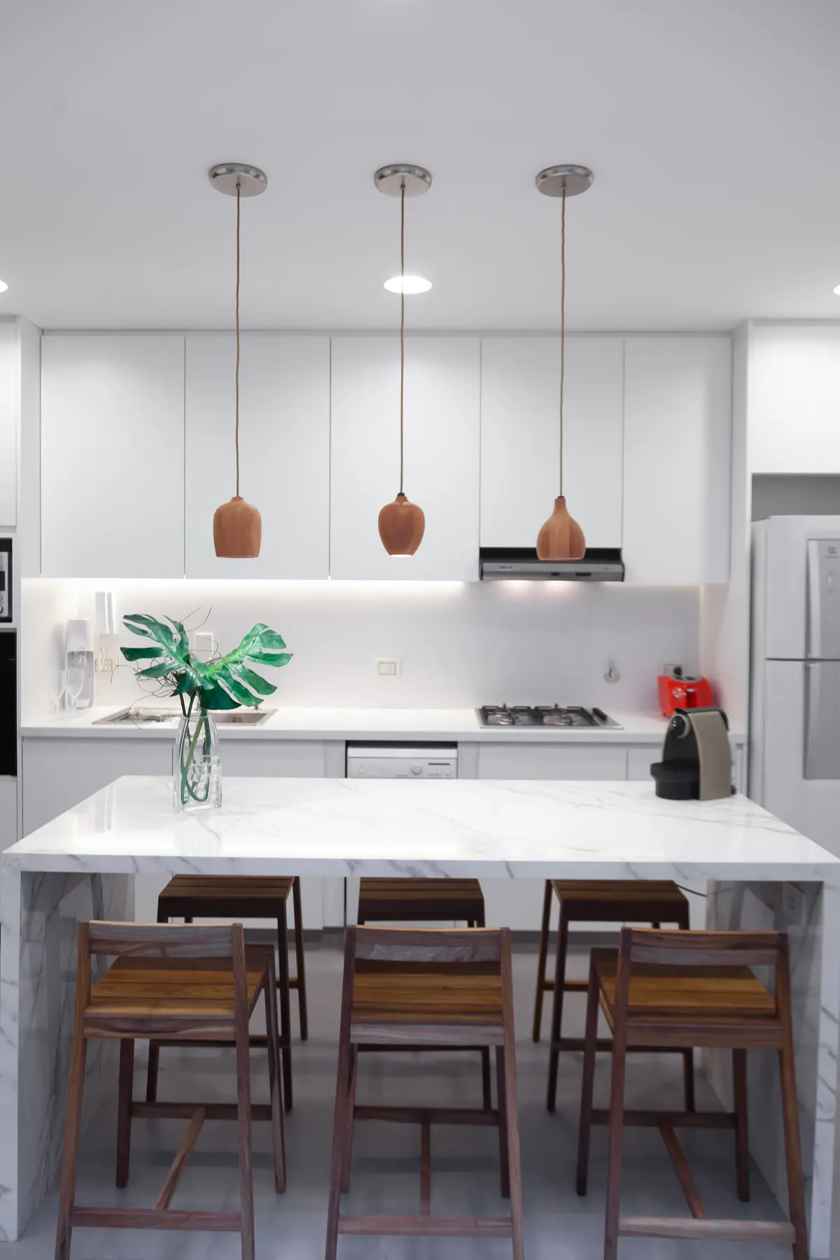 Cocina moderna con isla de mármol y taburetes, iluminación colgante — proyecto Obra Azcuenaga MI, por Arq. Lourdes Yarade Saravia, en Buenos Aires