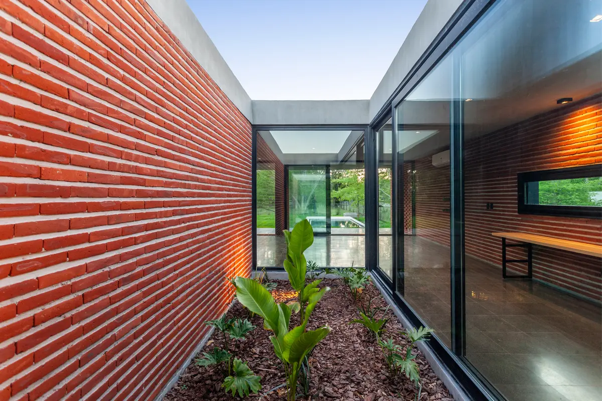 Pátio moderno com parede de tijolos aparentes e janelas de vidro — projeto Casa FLOIG, por V2 Arquitectos, em Villa Elisa
