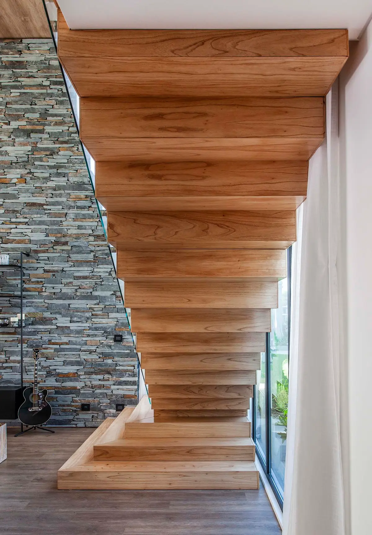 Escada moderna flutuante de madeira ao lado de parede de pedra empilhada — projeto CASA T199, por A'PRIMA - Arquitectura Sustentable, em Los Robles 5901